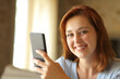 © Antonioguillem - Happy woman holding phone looks at camera at home