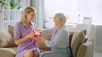 young blonde gives small box with present to aged lady with joyful smile