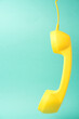 Retro yellow telephone receiver on a turquoise blue background, space for text.