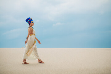 Wall Mural - Woman in image of egyptian queen Nefertiti walks through sandy desert.