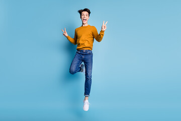 Sticker - Full length photo of cool brunet young guy jump show v-sign wear sweater jeans isolated on blue color background