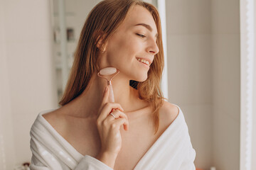 Wall Mural - Woman doing self massage with rose quartz face roller