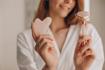 Woman making massage with gua sha stone and face roller