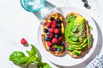 Poster - Peanut butter and berries toast and avocado toast with basil on white plate. Healthy vegan breakfast concept.