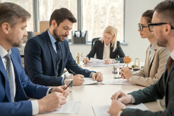 Poster - Group of business people sitting at the table and making notes at the table during a business meeting at office