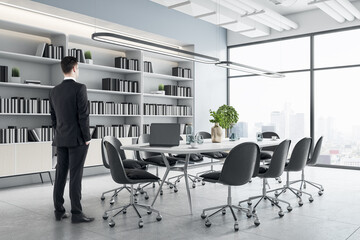 Poster - Businessman standing in modern meeting room interior with furniture, bookcase and city view. Corporate workplace and ceo concept.