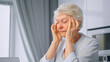 © AboutLife - Old tired of work lady pensioner with short grey hair massages temples with hands
