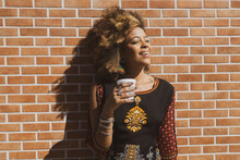 Beautiful African American Woman Leaning Against  Orange Bricks Wall Taking A Break Holding A Cup Of Coffee Looking Away. Copy Space For Text.