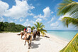 People riding horses on a tropical beach, Mexico. In the background the blue sky and the Caribbean Sea