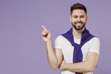 Wall Mural - Happy cheery young brunet man 20s wear white t-shirt purple shirt pointing on workspace area copy space mock up isolated on pastel violet background studio portrait. People emotions lifestyle concept