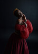 © faestock - Classical  portrait of pretty African woman wearing red renaissance medieval fantasy gown,  shadowy lighting on a dark studio background.