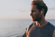 © ViDi Studio - Close up side view young strong athletic toned fit sportsman man in sports clothes earphones warm up train with music at sunrise sun dawn over sea beach outdoor on pier seaside in summer day morning