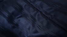 Close Up Dark Blue Satiny Blanket Or Silky Fabric Background With Beautiful Creased Pattern. Crumpled Dark Blue Silk Bed Sheet Background. Close Up Of Rippled Navy Fabric.