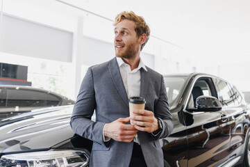 Canvas Print - Man minded customer male buyer client in suit choose auto hold cup drink coffee to go look aside want buy new automobile in car showroom vehicle salon dealership store motor show indoor Sales concept