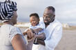 © Sabrina - African american parents having fun with toddler in summer vacation on the beach - Family love