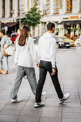 Wall Mural - Back view of happy couple holding hands and walking down street, romantic walk. Lifestyle concept