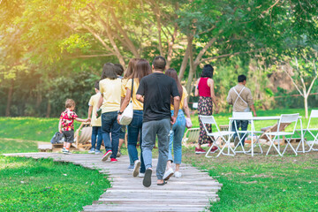 Back view of Asian man walking on pathway through green garden. Group of people walking together in park. Happy friends spending time together outside in green nature. Enjoying nature outdoors.