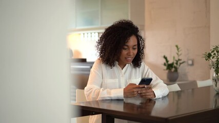 Poster - Joyful young mixed race woman chatting use smartphone enjoying break during work in front of laptop. Smiling female typing message or texting on mobile sitting on desk at home office