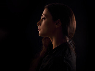 Beautiful serious concentration intelligence business woman in darkness with thinking look in the future on black background. portrait in dark shadow low key. Art. Profile