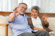 © comzeal - Happy elderly Asian couple smiling positive doing ok sign in living room at home