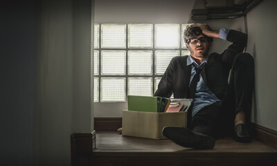 Depressed Umemployed Business office worker is sitting with card box in narrow dark stair for getting fired concept.