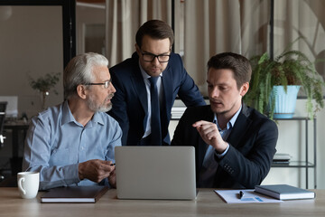 Poster - Male business team working on project together, meeting and talking at computer. Office employees of different generations watching and discussing content on laptop, sharing workplace for teamwork