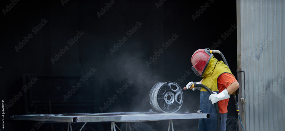 Caucasian man dressed in special protective equipment using sandblaster for cleaning metal details at work. Concept of people and repairing. - obrazy, fototapety, plakaty 