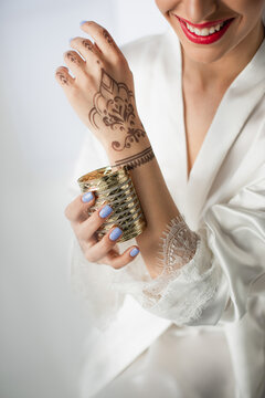 cropped view of happy indian woman with mehndi on hand wearing bracelet on grey