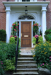 Poster - Portico entrance with elegant wood grain front door surrounded by colorful summer flowers