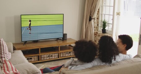 Sticker - Composite of happy family sitting at home together watching running athletics event on tv