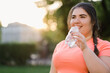 Water detox. Body refreshment. Diet nutrition. Body positive. Happy young overweight obese woman drinking from bottle in defocused copy space sunset park.