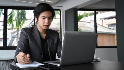 Wall Mural - Serious businessman working with laptop computer and making note on notebook.