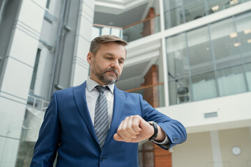 Aufkleber - Mature bearded businessman in suit checking his time while standing against the office building, he hurrying to work