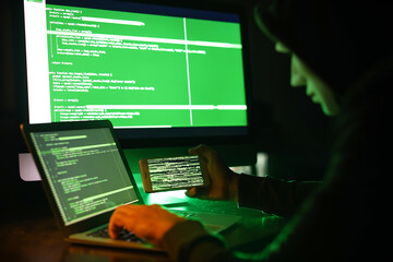 Hacker with mobile phone using computer in dark room