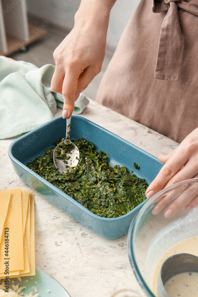 Woman preparing tasty green lasagna in kitchen