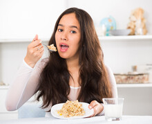 Young Smiling Girl Eating Tasty Mixture Of Cereals Sitting On The Table