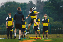 Teenage Football Players Training Headshots  Young Player Jumping High And Head Ball. Coach Coaching Junior Youth Football Club. Soccer Training Equipment On Grass Field