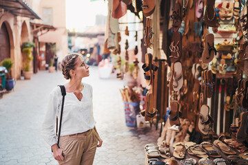 Wall Mural - Travel and shopping. Young traveling woman with choose presents in shoes shop in Morocco.