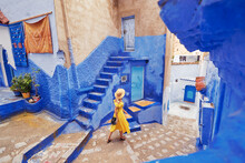 Colorful Traveling By Morocco. Young Woman In Yellow Dress Walking In  Medina Of  Blue City Chefchaouen.