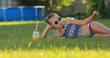 Teen Girl In A Swimsuit And Sunglasses Is Eating Pizza At Green Lawn While Summer Picnic. On The Background Of The Pool. Summer Vacation Activity