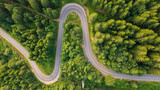 Fototapeta Uliczki - Aerial view of countryside road passing through the green forrest and mountain. Green pine and fir trees forest. Beautiful mountain road.