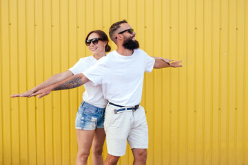 Wall Mural - Young smiling pretty happy cheerful positive couple in blank white t-shirts near color background on street. Mockup for design.