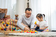 © ronnachaipark - Happy young father and mother and a little daughter playing with Toy wooden blocks, sitting on the floor in living room, family, parenthood and people concept with Developmental toys
