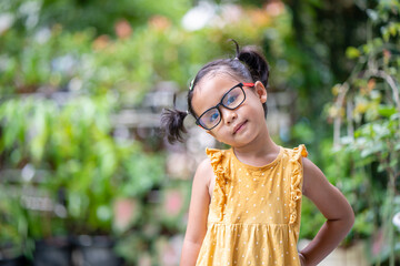 Wall Mural - Happy little girl with glasses standing at garden.