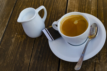 Poster - Top view of a cup of coffee with a plate and a white milk jug on the wooden background