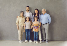 Studio Photoshoot Group Portrait Of Happy Big Extended Multi Generational Family. Cheerful Mom, Dad, Grandma, Grandpa And Two Little Daughters With Toy Standing Together, Looking At Camera And Smiling