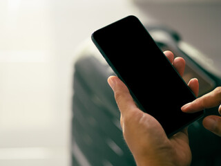 Wall Mural - hand holding of a smartphone with suitcase background. close-up photo. space for text. technology an