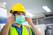 © winnievinzence - Male engineer worker wearing protective face mask, safety helmet and glasses at factory. industrial plant and new normal working. man standing and look forward, copy space