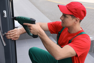 Poster - Handyman with screw gun repairing door lock outdoors