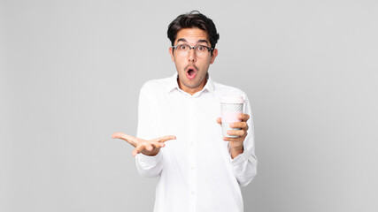 young hispanic man feeling extremely shocked and surprised and holding a take away coffee